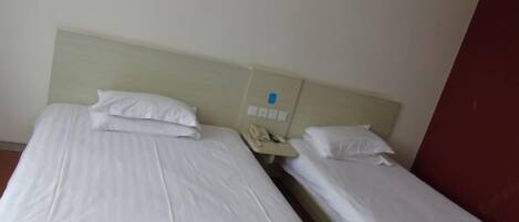 Two single beds with white linens, a bedside telephone, and a red wall.
