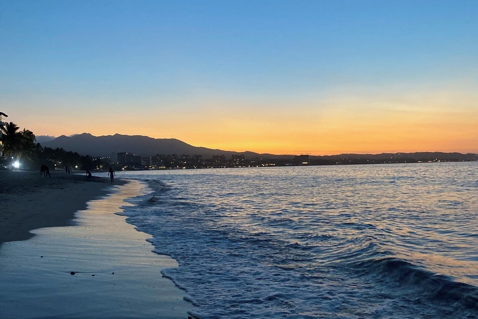 A beach with a calm sea, a clear sky, and distant mountains.
