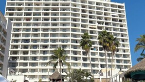 Ein mehrstöckiges Hotel mit Balkonen, Palmen und blauem Himmel.