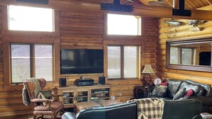 A cozy log cabin interior with a wooden ceiling, a large TV, a leather sofa, and a fireplace. - Charming 3-bedroom cabin in Victor only 25 miles from Jackson Hole, pet friendly (Victor)