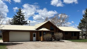 A two-story log cabin with a garage, surrounded by a gravel driveway and sparse vegetation. - Charming 3-bedroom cabin in Victor only 25 miles from Jackson Hole, pet friendly (Victor)