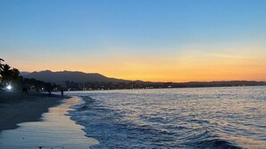 Een strand met een rustige zee, een heldere lucht en verre bergen.