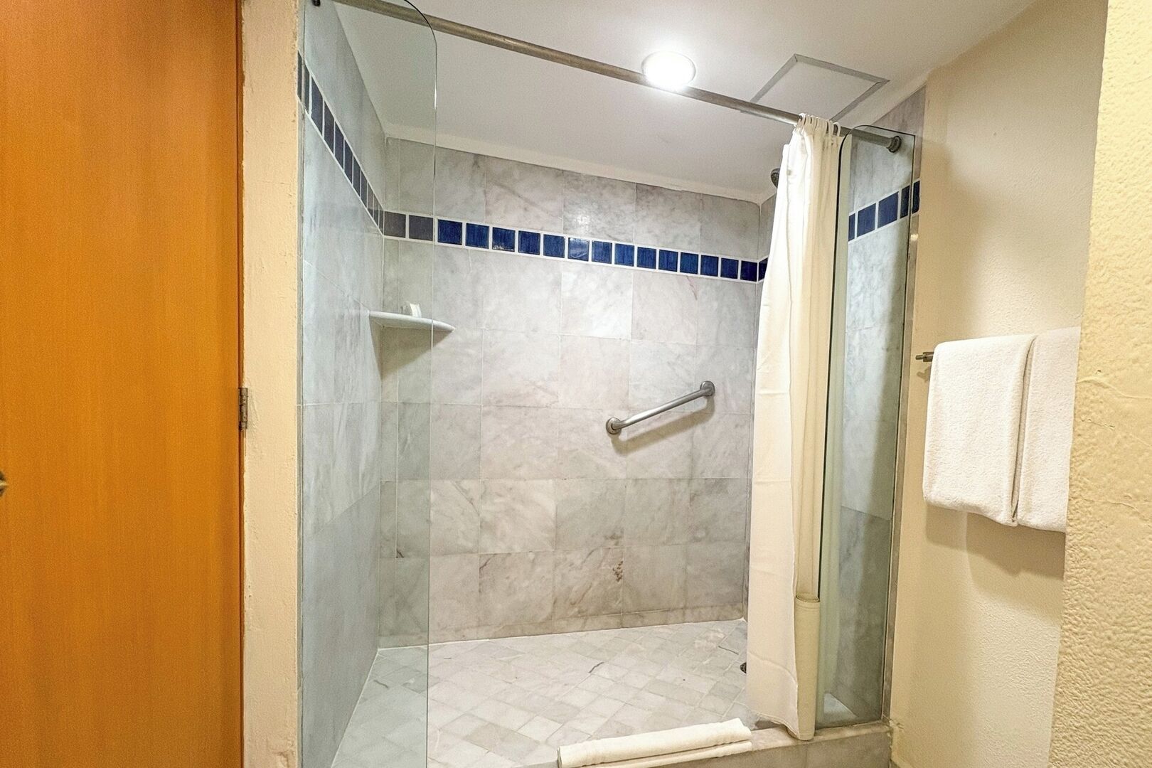 A glass-enclosed shower with a white tiled floor and a blue-tiled accent wall.