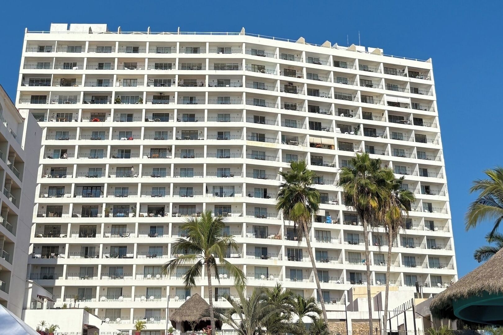 A multi-story hotel with balconies, palm trees, and a clear blue sky.