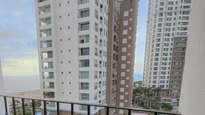 A high-rise residential building with multiple balconies, a view of the sea, and a clear sky.