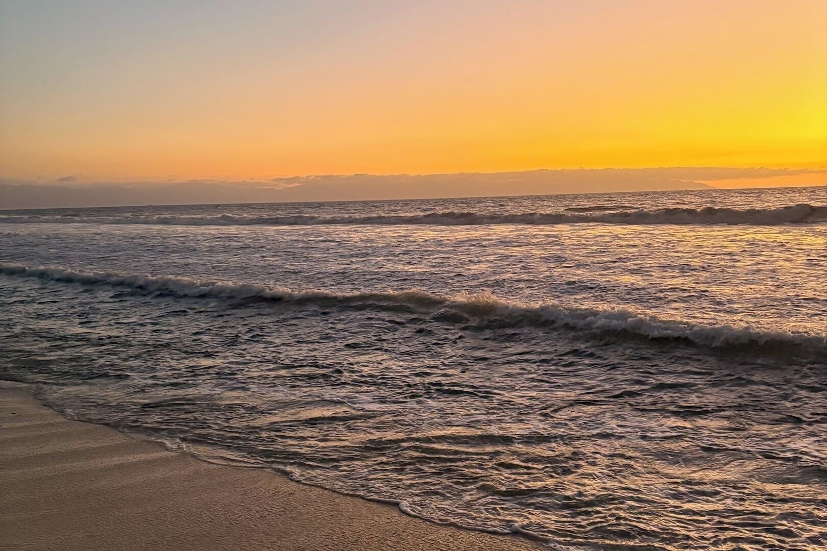 Een strand met golven bij zonsondergang.