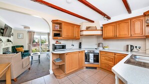 A compact kitchen with wooden cabinets, a microwave, oven, and a sink. - Cottage in Thirsk With Private Hot Tub (Thirsk)