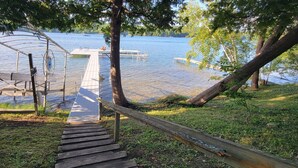 Eine Holztreppe führt zu einem Steg über dem Wasser, umgeben von Bäumen und Gras.