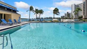 A swimming pool with clear blue water, surrounded by lounge chairs and palm trees.