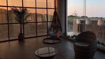 A spacious room with large windows, a hanging chair, a round table, and two wicker chairs.