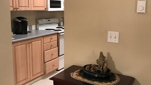 Eine Küche mit Holzausstattung, einer Mikrowelle, einem Herd und einer Kaffeemaschine. An der Wand hängt ein Gemälde und es steht ein kleiner Tisch mit einer Dekoration darauf.