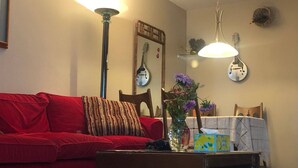 Ein Wohnzimmer mit einem roten Sofa, einem Holzstuhl, einem Tisch mit Blumen und einer Lampe.