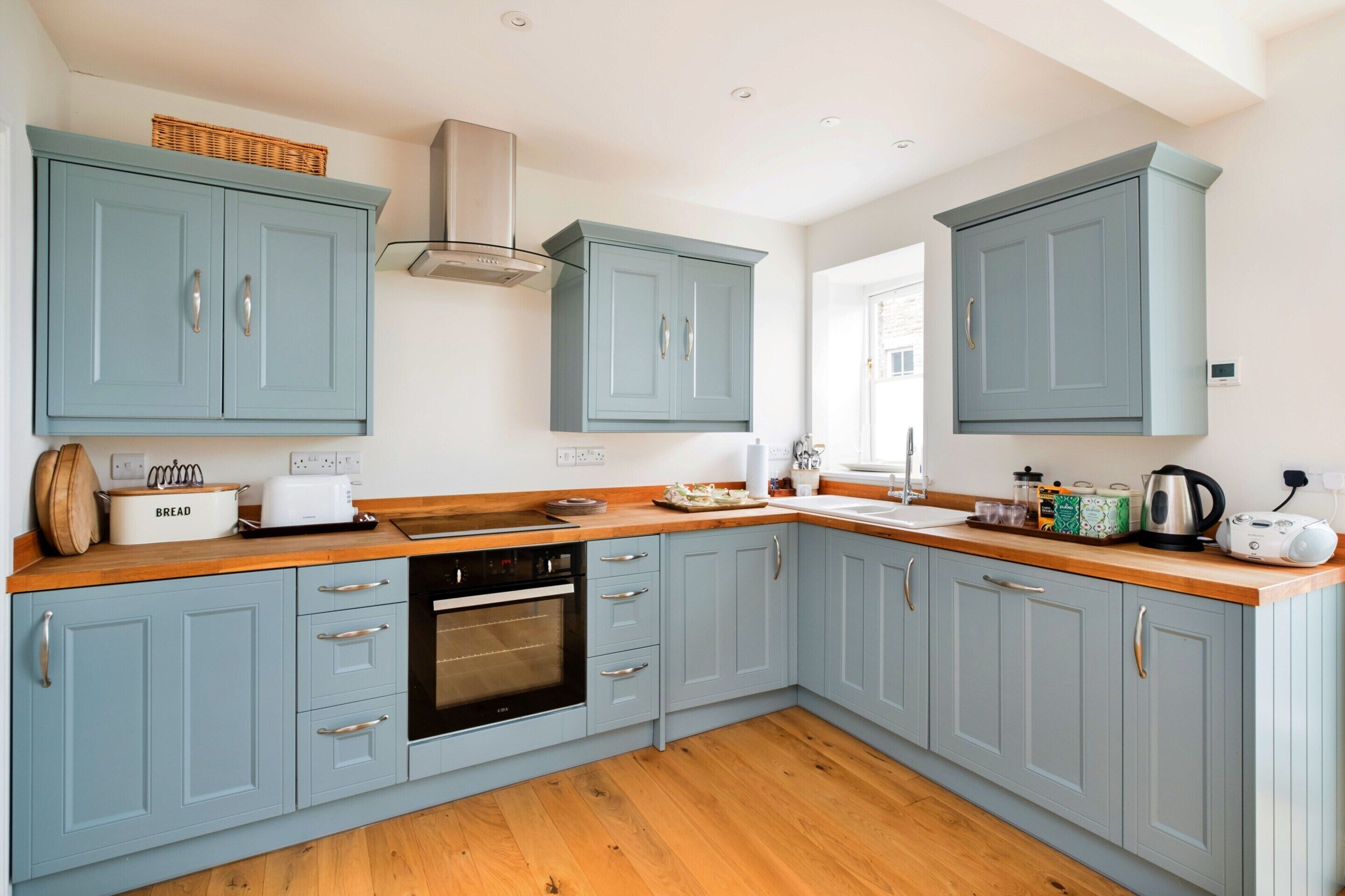 A kitchen with light blue cabinets, a wooden countertop, a built-in oven, and a visible window.