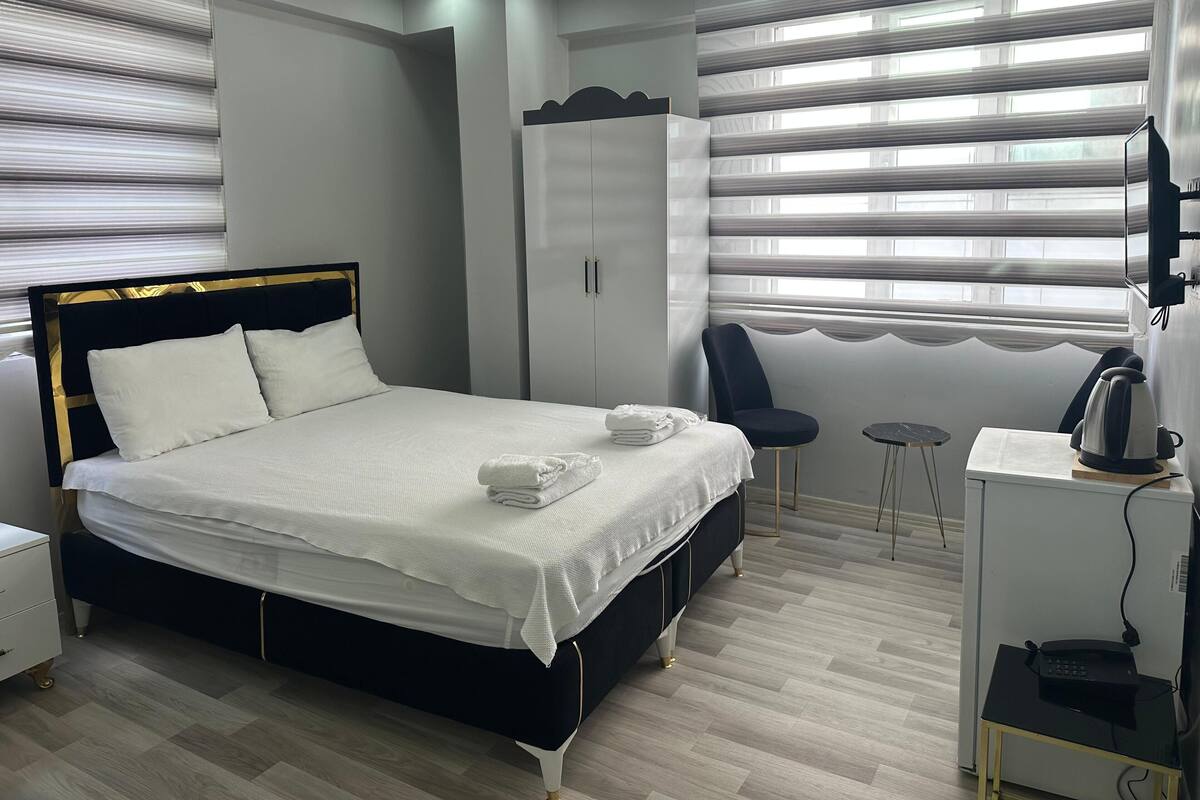 A modern hotel room with a bed, a wardrobe, a desk with a kettle, and a chair.