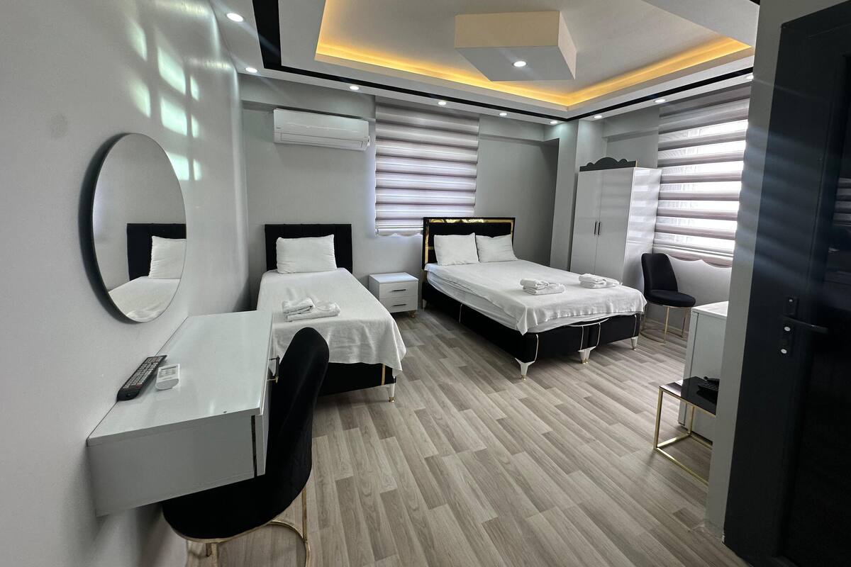 A modern hotel room with two beds, a desk, a chair, a wardrobe, and a mirror.