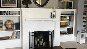 Een woonkamer met een witte schoorsteen, boekenplanken, een wereldbol en een ingelijst kunstwerk aan de muur.