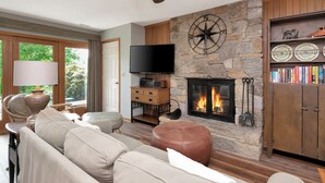 A living room with a stone fireplace, a television, and a bookshelf. - Aspen 2 | Fireplace, Restaurant, Pool, Spa (Blowing Rock)