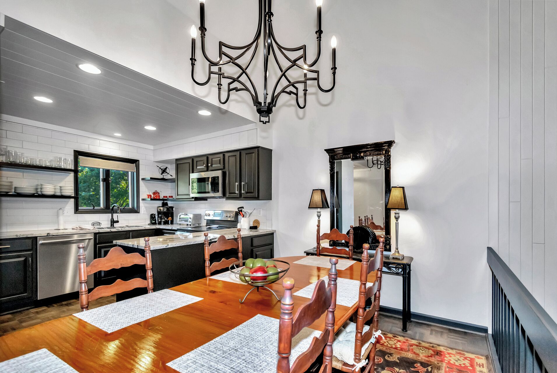 A modern kitchen with dark cabinets, a stainless steel refrigerator, and a dining area with a wooden table and chairs.
