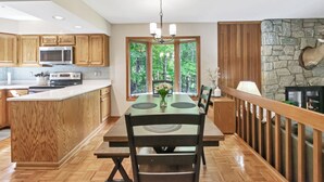 A kitchen with wooden cabinets, a built-in microwave, a dining table with chairs, and a stone fireplace.