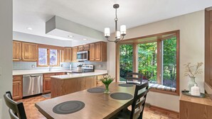 A modern kitchen with wooden cabinets, a central island, and a dining area with a view of greenery.