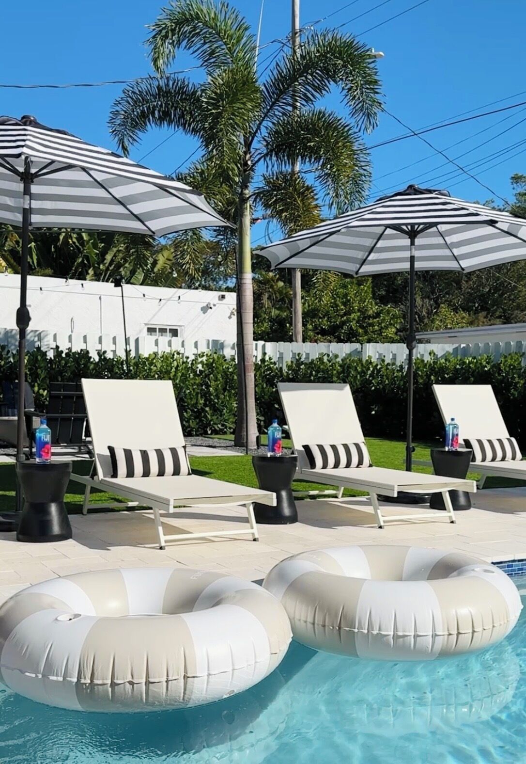 A poolside area with lounge chairs, striped umbrellas, and inflatable shark floats.