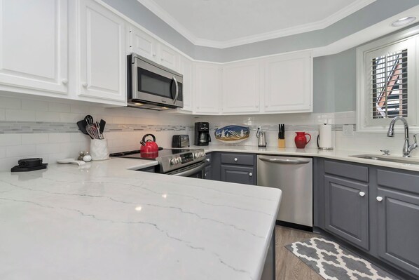 A modern kitchen with white cabinets, a stainless steel microwave, a red kettle, and a coffee maker.