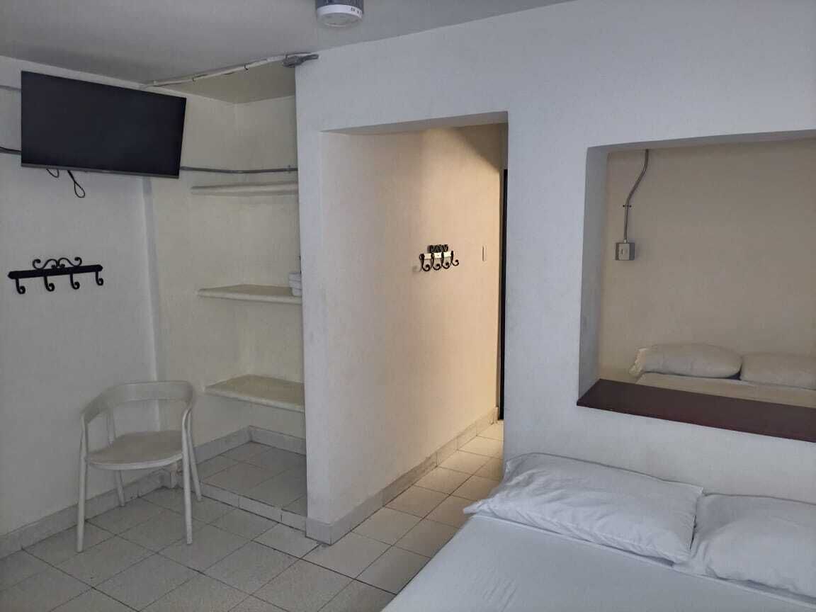 A room with a bed, a TV mounted on the wall, a chair, and a shelf with a mirror.