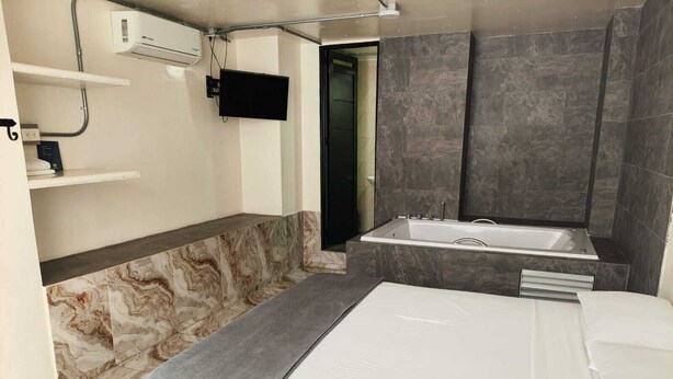 A modern bathroom with a bathtub, a shower, a toilet, and a TV mounted on the wall. - Hotel Villanueva Comfort (Medellín)