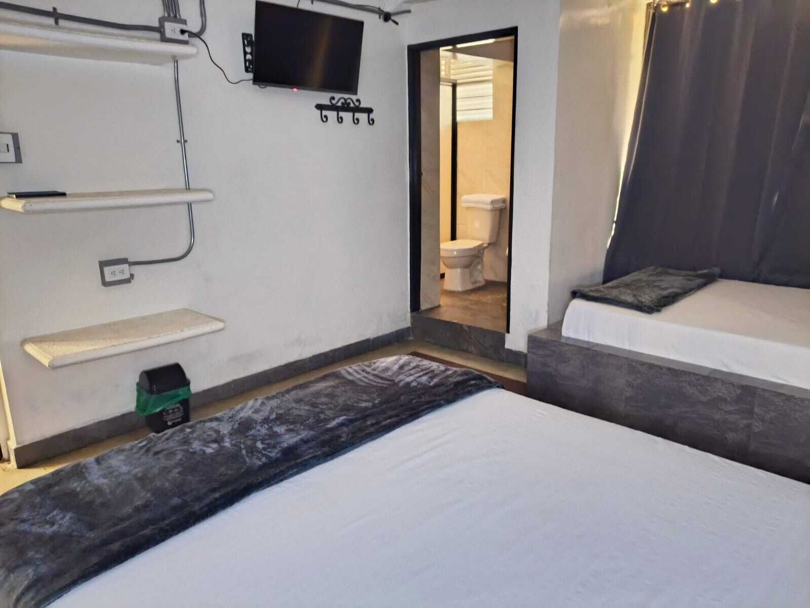 Een slaapkamer met een bed, een aan de muur bevestigde televisie, een klein plankje en een deur naar een badkamer.
