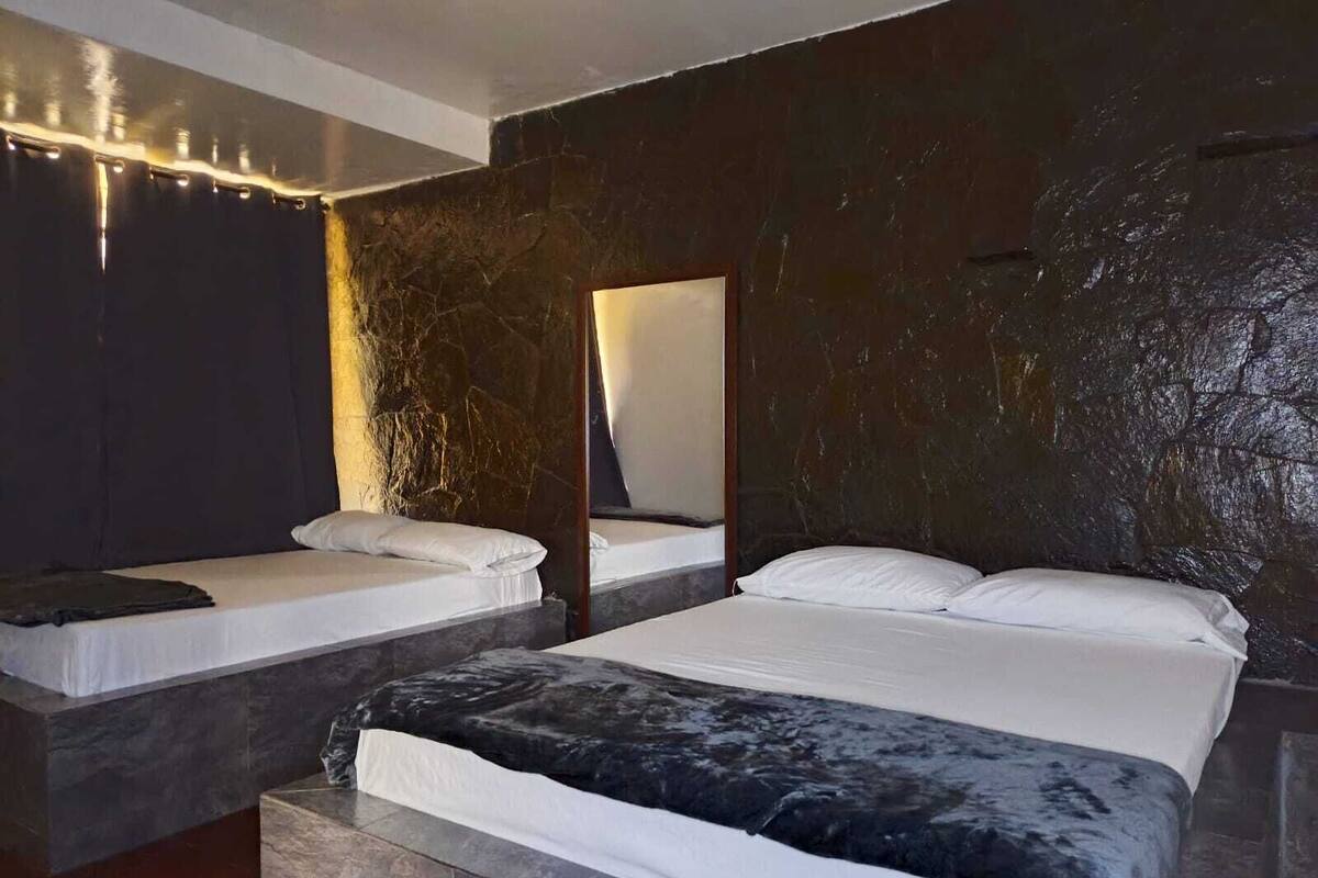 Une chambre moderne avec un grand lit, deux petits lits et un mur en pierre.