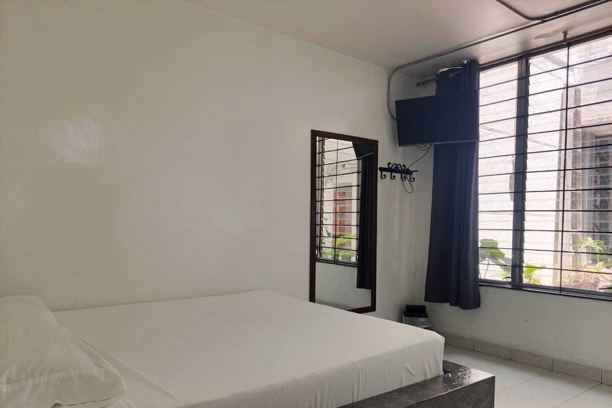 Une chambre à coucher avec un lit, une fenêtre avec des barreaux en métal, un rideau et un climatiseur fixé au mur.
