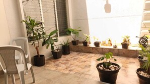 A patio area with potted plants, a white chair, and a window with blinds. - Hotel Villanueva Comfort (Medellín)