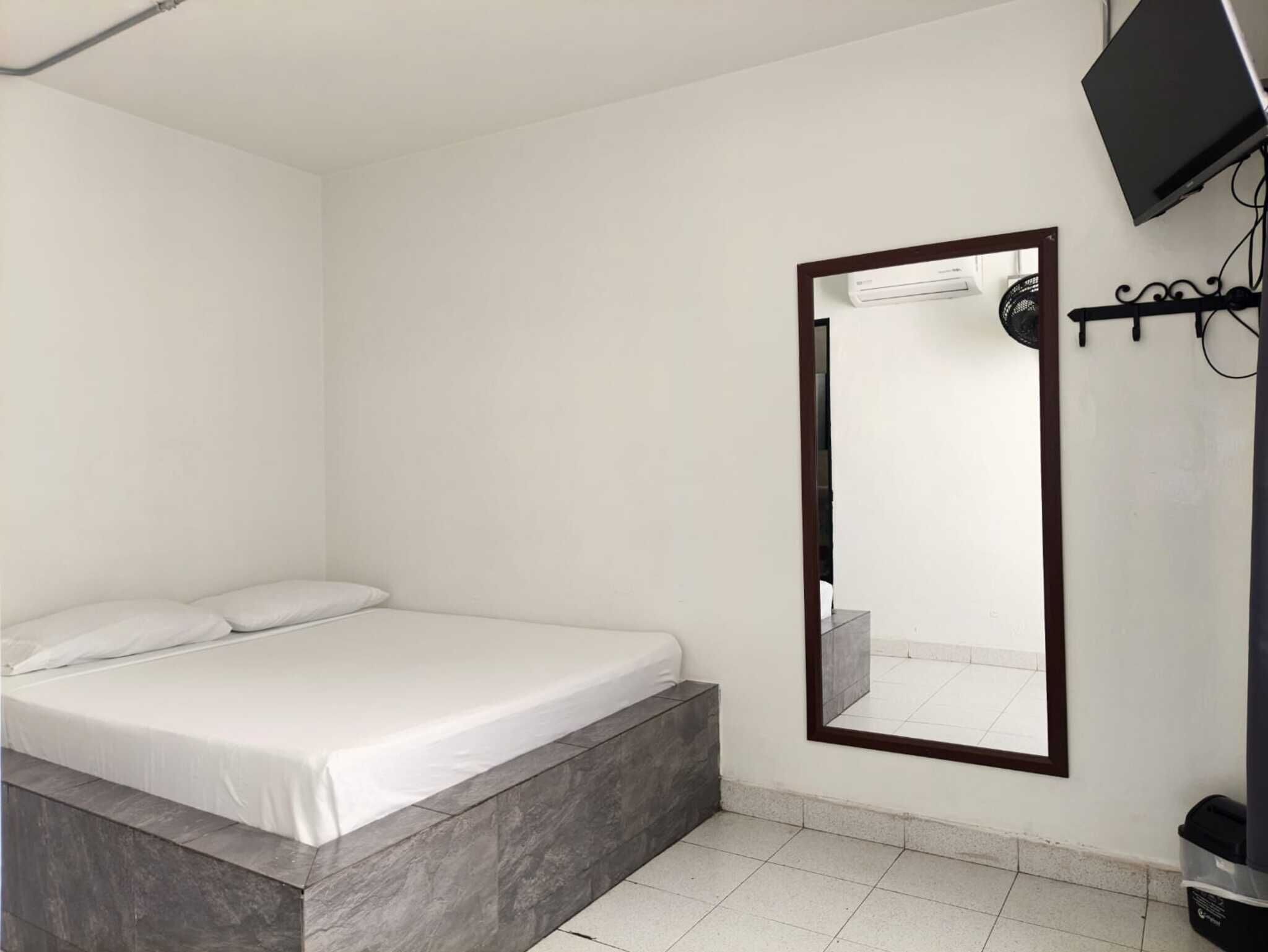 Ein Schlafzimmer mit einem Bett, einem großen Spiegel, einem Fernseher und einem Wandheizkörper.
