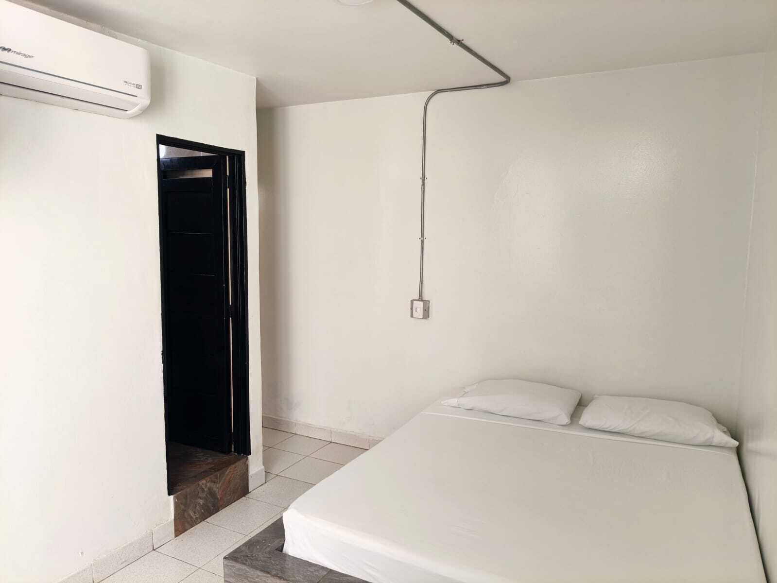 Quarto com cama, parede branca, porta e ar condicionado.