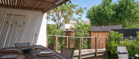 A wooden deck with a table set for dining, surrounded by a wooden fence and greenery.