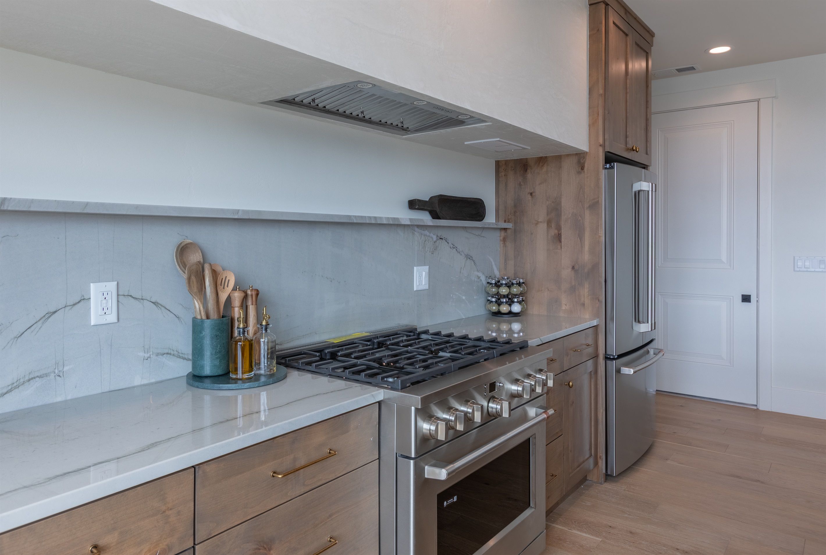 Een moderne keuken met een roestvrijstalen fornuis, oven en koelkast, houten kastjes en marmeren aanrechtbladen.