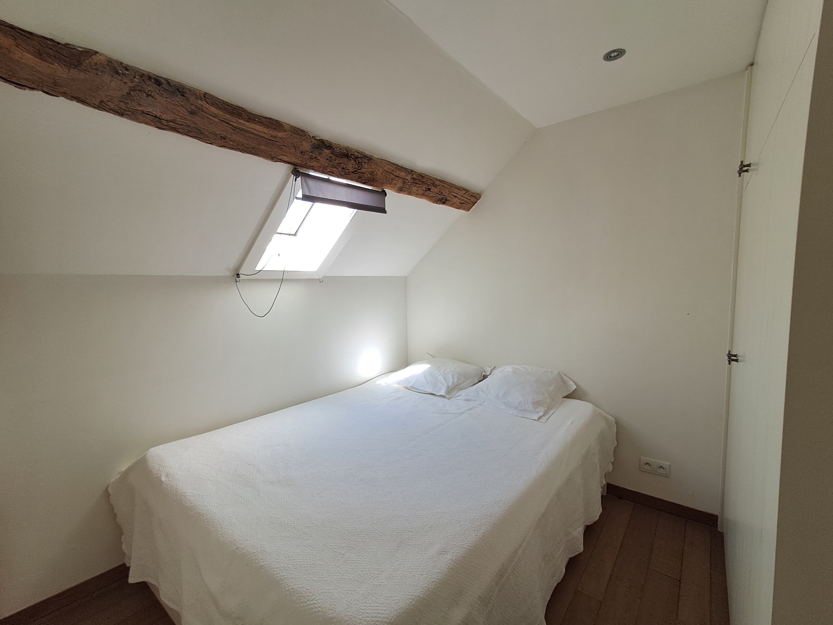 A small, single-bed room with a sloped ceiling and a skylight.