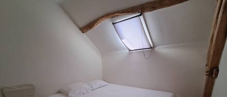 A small, white, single-bed room with a sloped ceiling and a window.