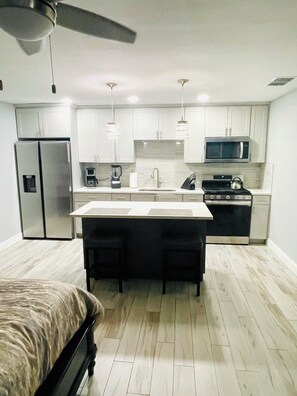 A modern kitchen with white cabinets, a refrigerator, a microwave, a stove, and a ceiling fan.