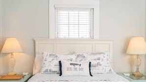 A neatly arranged bedroom with a bed, two bedside tables, a window, and a lamp on each side.