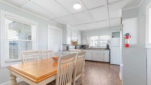A modern kitchen with white cabinets, a wooden dining table, and a fire extinguisher mounted on the wall.