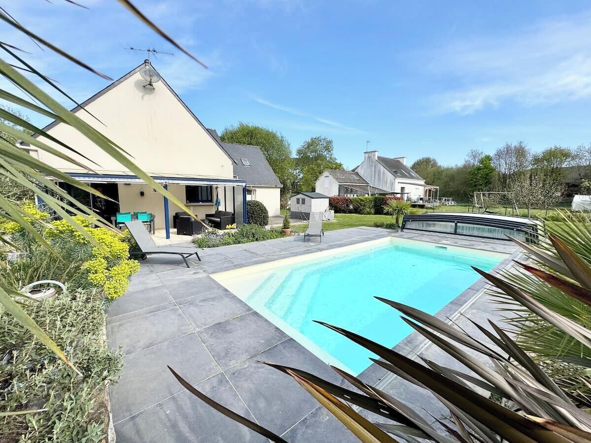 A swimming pool with a surrounding patio area, a covered seating area, and a house in the background.