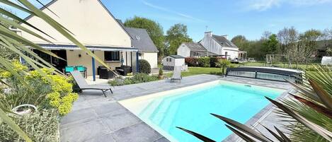 A swimming pool with a surrounding patio area, a covered seating area, and a house in the background.