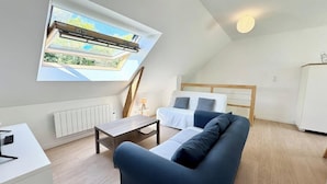 A modern, well-lit room with a sloped ceiling, a large skylight, a sofa, a coffee table, and a radiator.