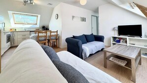 A modern, well-lit room with a sofa, a coffee table, a TV, and a dining area with a table and chairs.