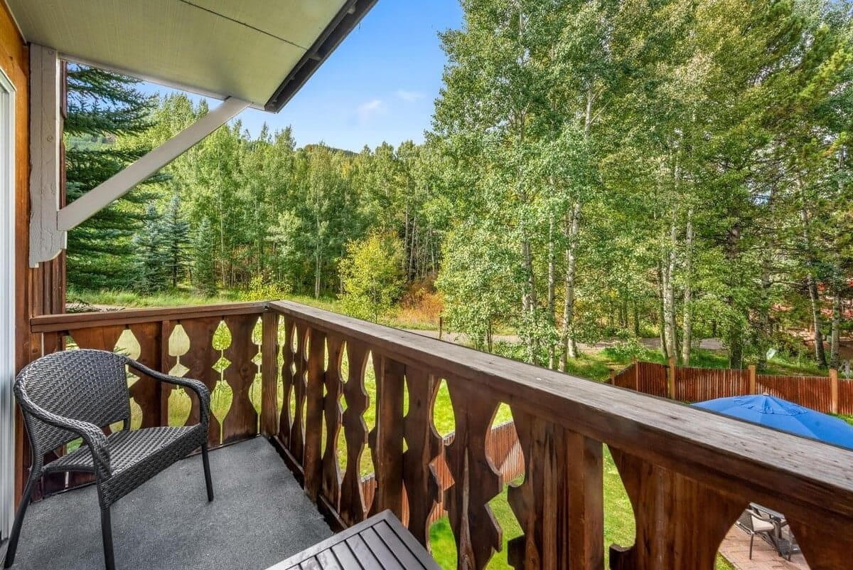 A wooden deck with a chair and a table, overlooking a forested area.