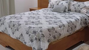 A bedroom with a wooden bed, white bedding with a floral pattern, and beige curtains. - Stay at luxurious exclusive condo 10 minute walk from caleta beach  (La Romana)