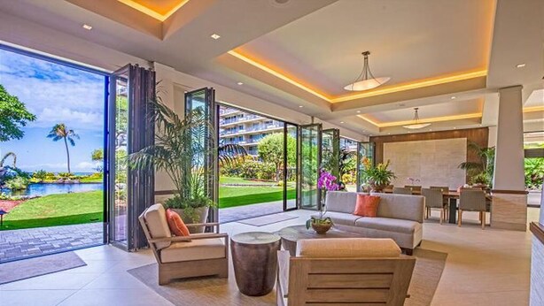 Eine moderne Hotellobby mit einer großen Glaswand, die einen Blick auf ein Schwimmbad und Grünflächen bietet. Es gibt eine Sitzecke mit einer Couch und Sesseln sowie einen kleinen Tisch mit einem Blumenstrauß.