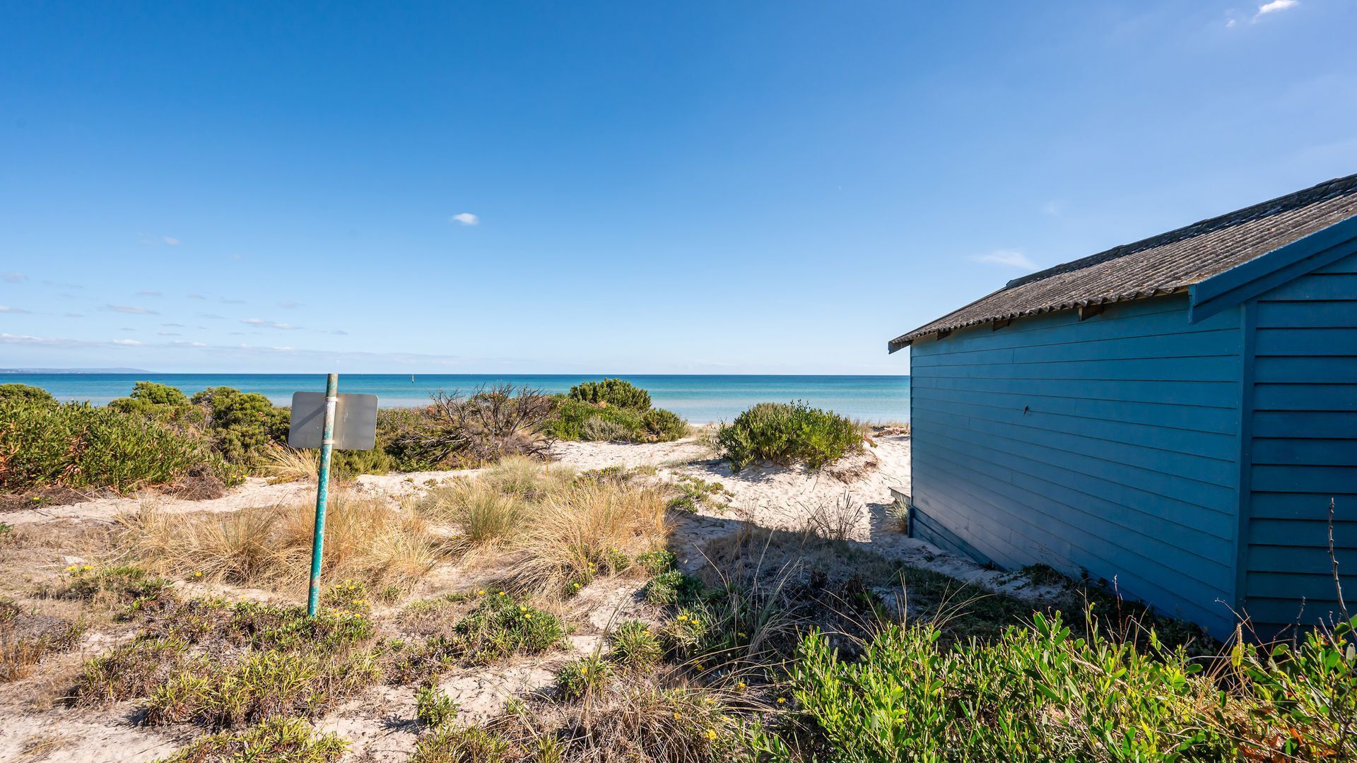 Una casa frente al mar con un sendero de arena que lleva al océano, rodeada de vegetación.