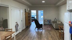 A spacious living area with a wooden floor, a black armchair, a sofa, a dining table with chairs, and a kitchen area with a refrigerator. - New 2 bedroom apartment in Toronto 
782 St. Clair ave.west (Toronto)